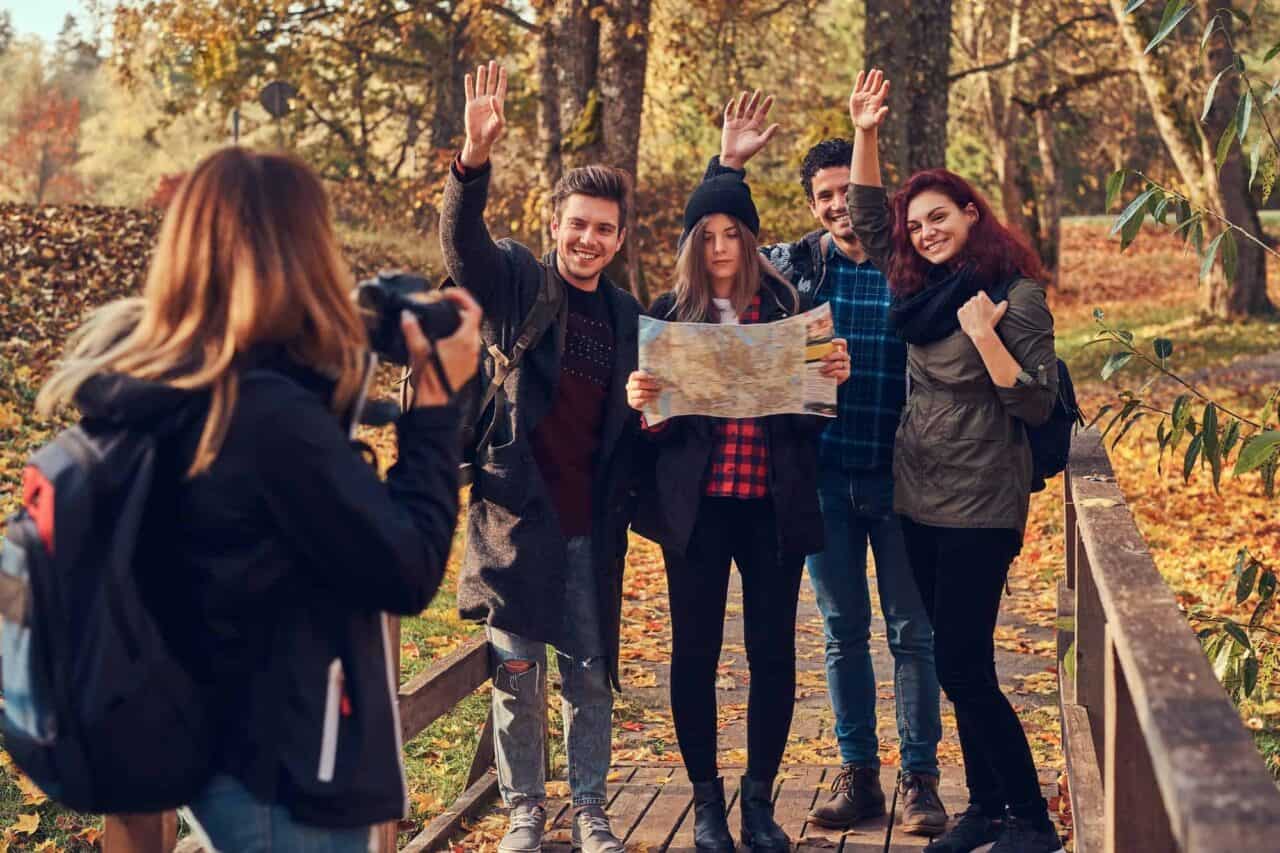 Girl taking a photo of her friends. Group of young friends hiking through forest.