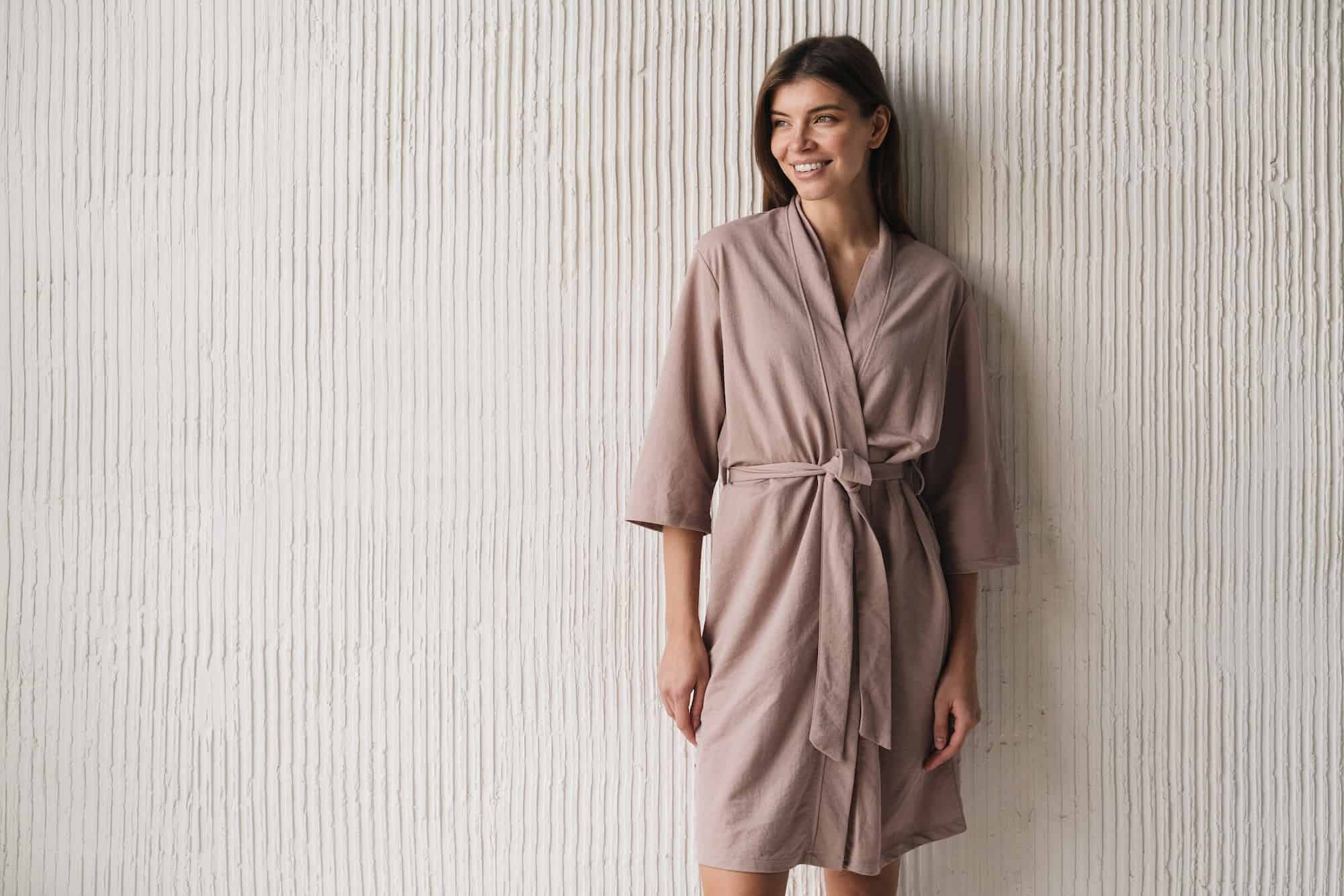 Portrait of woman in silk dressing gown standing near textured wall